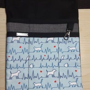 Könnte beinhalten: Ein schwarzer Stoff-Utility-Gürtel mit einer blauen und weißen gemusterten Tasche. Die Tasche hat ein sich wiederholendes Muster aus weißen Silhouetten von Katzen, Hunden und Vögeln mit roten Herzen und blauen EKG-Linien. Der Gürtel hat ein graues Stoffband und einen silbernen Metallclip.