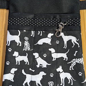 Könnte beinhalten: Schwarzer Canvas-Utility-Gürtel mit mehreren Taschen und einem Hunde-Druckmuster. Der Gürtel hat einen weißen Tupfen-Besatz und einen silbernen Clip.