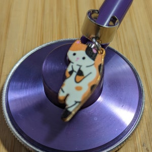 May include: Purple stethoscope with a silver ring and a charm of a cartoon cat with orange, black, and white markings.