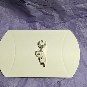 May include: A silver ear cuff with a dangling charm of a white cat with gray markings. The cat is facing to the left and has a surprised expression.