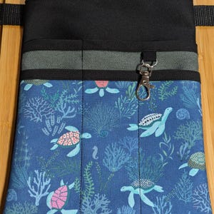 Könnte beinhalten: Ein blauer Werkzeuggürtel aus Stoff mit mehreren Taschen und einem silbernen Clip. Der Stoff hat ein Muster aus Meeresschildkröten, Korallen und Algen.
