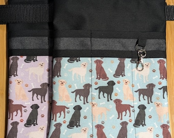 May include: Two black canvas utility belts with multiple pockets. The belt on the left has a purple and white pattern with black labrador retrievers and bones. The belt on the right has a blue and white pattern with black, brown, and yellow labrador retrievers and bones.