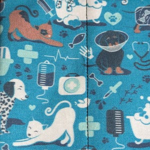 May include: Blue fabric with a repeating pattern of white and black dogs, cats, and medical symbols. The fabric has a black seam down the center.