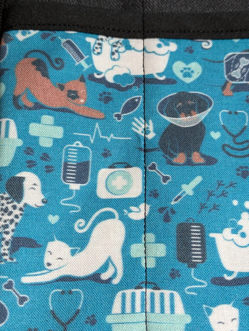 May include: Blue fabric with a repeating pattern of white and black dogs, cats, and medical symbols. The fabric has a black seam down the center.