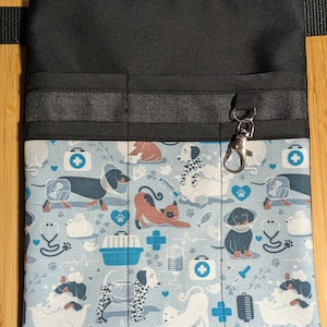 May include: Black utility belt with multiple pockets and a clip-on hook. The belt is lined with a blue and white fabric featuring a pattern of dogs, cats, and veterinary symbols.