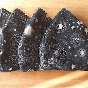 May include: Four black fabric face masks with a white celestial print. The print features suns, moons, stars, and clouds.