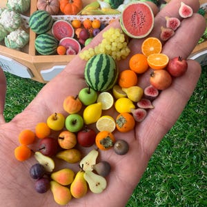 Pu&ograve; includere: Una collezione di repliche di frutta in miniatura che include piccole angurie, uva, arance, limoni, mele, pere, fichi e melograni. L'assortimento presenta frutti interi e affettati in vari colori come verde, rosso, giallo e arancione.