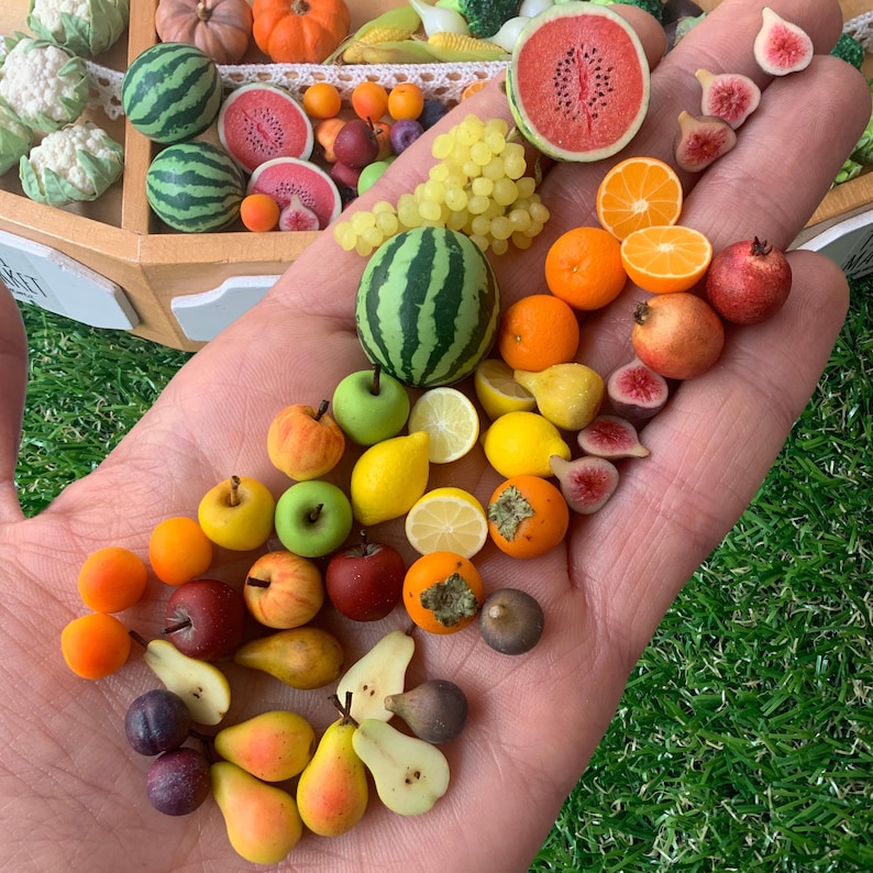 Pu&ograve; includere: Una collezione di repliche di frutta in miniatura che include piccole angurie, uva, arance, limoni, mele, pere, fichi e melograni. L'assortimento presenta frutti interi e affettati in vari colori come verde, rosso, giallo e arancione.