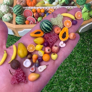 Könnte beinhalten: Eine Sammlung von Miniatur-Fruchtnachbildungen, darunter Wassermelonen, Bananen, Papayas, Weintrauben, Orangen, Zitronen, Granatäpfel, Feigen und eine Kokosnusshälfte. Diese kleinen, detaillierten Objekte zeigen eine Vielzahl von Farben und Texturen.