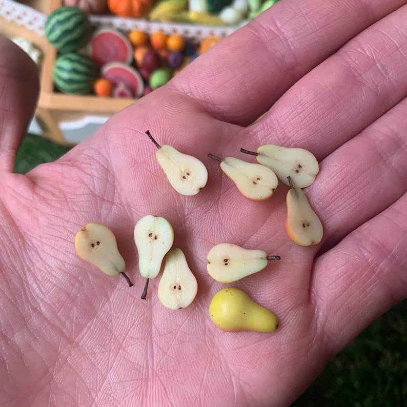 Pu&ograve; includere: Una collezione di pezzi di pera in miniatura, tra cui diverse met&agrave; che mostrano la polpa chiara e minuscoli semi marroni, e una piccola pera gialla intera. Queste minuscole repliche di frutta sono realizzate con dettagli realistici.