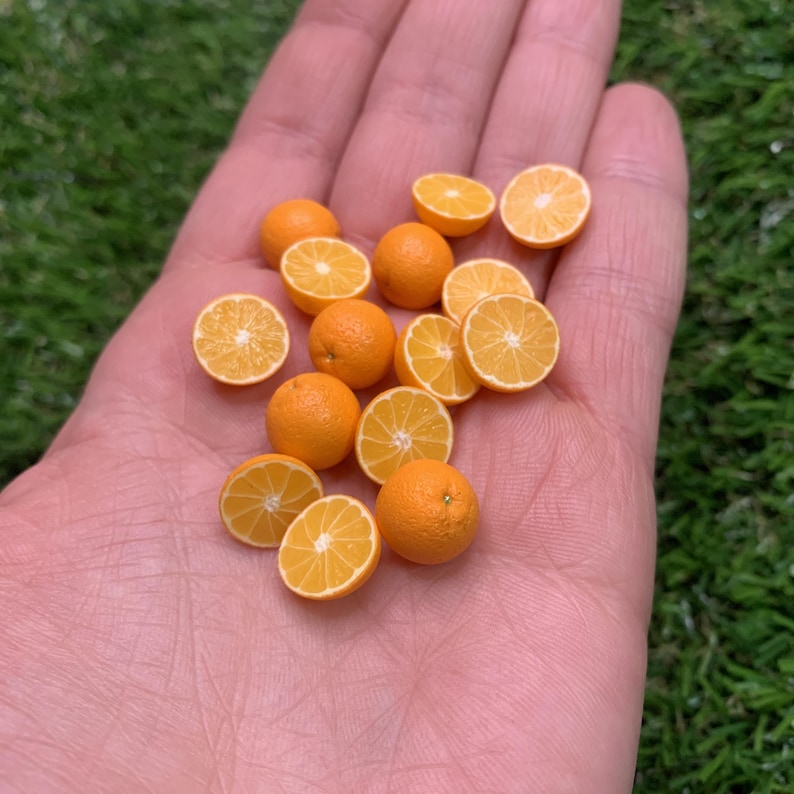 Pu&ograve; includere: Una collezione di repliche in miniatura di frutti arancioni, che include diverse piccole sfere intere e molteplici segmenti tagliati a met&agrave; che mostrano dettagliate texture della polpa in vivaci tonalit&agrave; arancione e giallo brillante.