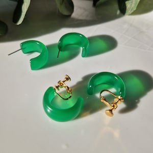 May include: A pair of green clip-on earrings. The earrings are made of a smooth, translucent material and have a simple, curved design.