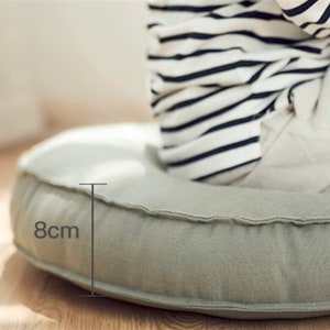 May include: A light green round floor cushion with 8cm thick padding. The cushion is made of a soft fabric and has a simple design.