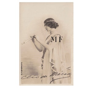 Pode incluir: Fotografia vintage em tons sépia de uma mulher em um vestido drapeado, segurando um instrumento longo e fino nos lábios. A imagem apresenta o texto "Cléo de Mérode" e outras escritas. A fotografia é da S.I.P. 60e Serie.