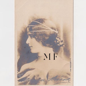 Pode incluir: Postal vintage em tons sépia com uma mulher em perfil. Ela usa uma faixa na cabeça e tem o cabelo preso em um coque. O postal tem as iniciais "MF" e uma assinatura. A imagem está em um cartão retangular.