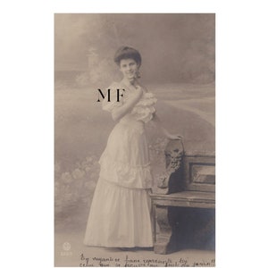 Vintage postcard, pretty young Victorian woman posing by a bench