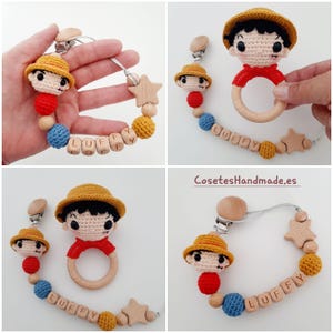 May include: A crocheted baby toy set featuring a character with a straw hat and red shirt. The set includes a teether, a rattle, and a clip-on toy with a wooden star and beads. The wooden beads are engraved with the name "LUFFY".