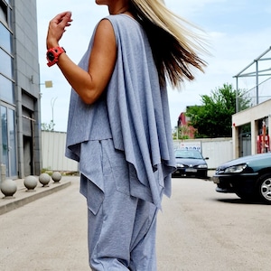 Puede incluir: Una mujer con un top gris sin mangas y pantalones a juego con un diseño suelto y fluido. Lleva zapatillas blancas con detalles rojos y tiene el pelo rubio.