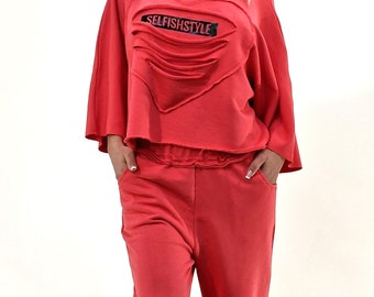 Peut inclure: Une femme portant une tenue rouge en deux pièces avec un détail en forme de cœur détérioré sur le haut. Le haut porte l'inscription "SELFISHSTYLE". La tenue est associée à des baskets blanches.