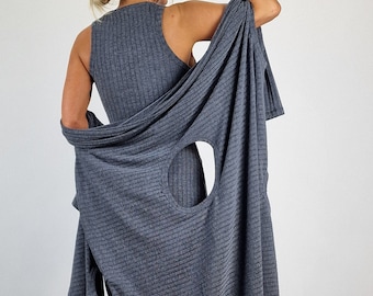 May include: A grey ribbed knit dress with a large circular cutout at the back. The dress is worn with a matching grey cardigan that is draped over the shoulders. The person is wearing pink trainers.