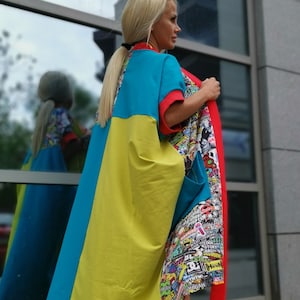 Puede incluir: Una mujer lleva un vestido largo y colorido con un estampado gráfico de varios adhesivos y logotipos. El vestido es azul, amarillo y rojo. Lleva zapatos de lona negros y blancos a cuadros.