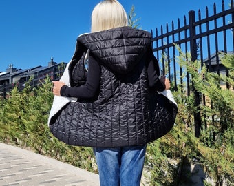 May include: A black quilted vest with a white sherpa lining and a hood. The vest is worn over a black long-sleeved shirt and blue jeans.