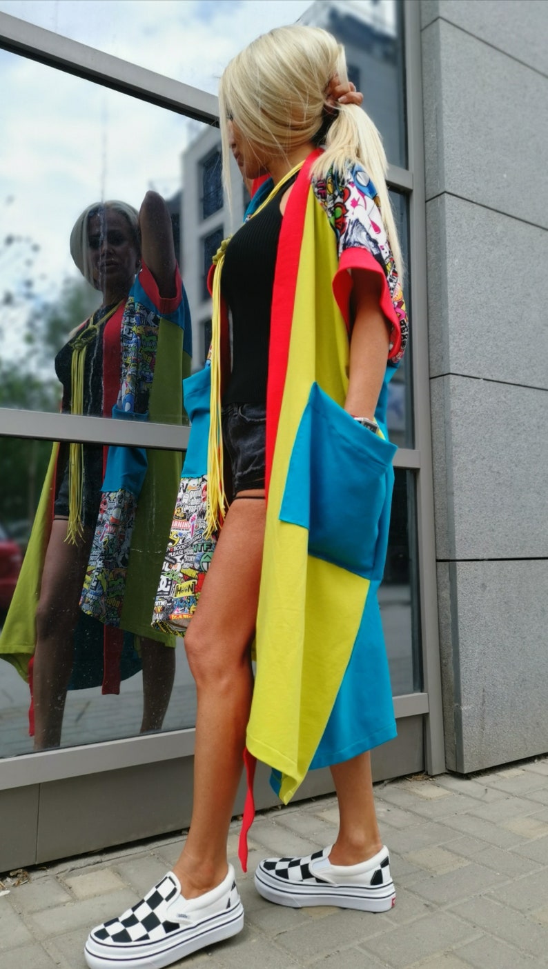 Może przedstawiać: Kobieta w kolorowej, wielobarwnej kurtce w stylu kimona z czarną bluzką i czarnymi spodenkami. Ma na sobie czarno-białe szachownice.