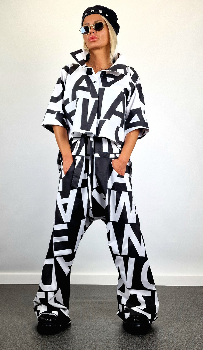 May include: A black and white patterned shirt and trousers set. The shirt is a cropped style with a button-up front. The trousers are loose-fitting with a wide leg. The model is wearing a black hat and sunglasses.