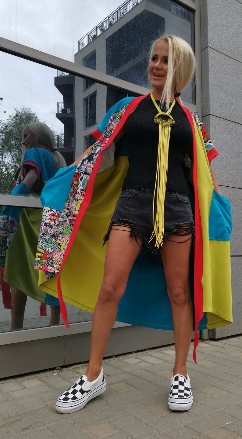 Może przedstawiać: Kobieta w kolorowym kimonie z wieloma wzorami, z ż&oacute;łtym naszyjnikiem z frędzlami, czarną koszulą na ramiączkach, podartymi dżinsowymi szortami i czarno-białymi sznurowanymi butami.
