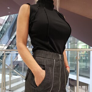 May include: A black mock neck sleeveless shirt with a ribbed texture and a denim skirt with multiple zipper details.