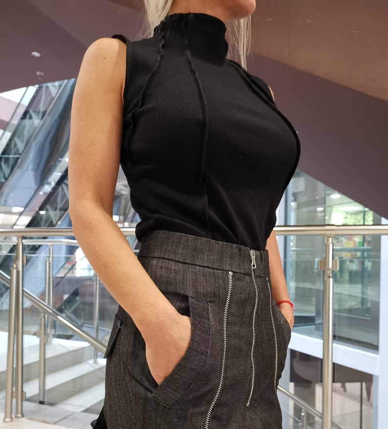 May include: A black mock neck sleeveless shirt with a ribbed texture and a denim skirt with multiple zipper details.