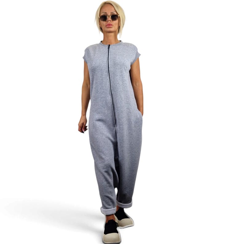 May include: A sleeveless light gray jumpsuit featuring a full-length front zipper closure, a round neckline, and cuffed ankles. The garment is made of a soft, heathered fabric and includes side pockets, providing a relaxed fit for casual wear.