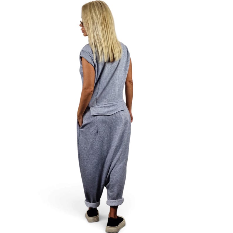 May include: A light gray sleeveless jumpsuit featuring a relaxed fit, a horizontal seam detail across the back waist, side pockets, and tapered legs with cuffed hems. The garment is constructed from a soft, jersey-like fabric with a smooth texture.