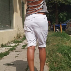 K&ouml;nnte beinhalten: Eine Frau tr&auml;gt ein graues T-Shirt mit Ausschnitten im R&uuml;cken und wei&szlig;e Shorts. Sie geht auf einem B&uuml;rgersteig.