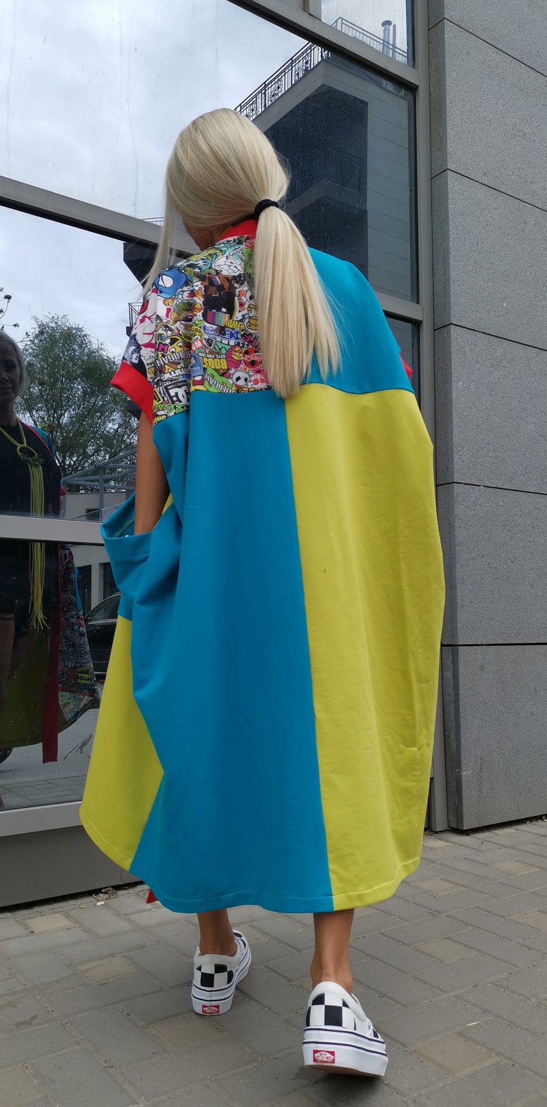 Może przedstawiać: Kobieta w niebiesko-ż&oacute;łtej sukience z kolorowym nadrukiem graficznym na plecach. Ma na sobie czarno-białe szachownice.