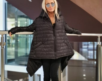 May include: A black quilted puffer jacket with a unique asymmetrical hemline and a hood. The jacket has a relaxed fit and is paired with black pants and sandals. The person is wearing sunglasses.