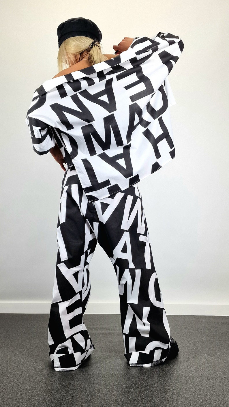 May include: A black and white patterned pantsuit with a black cap. The trousers are wide-legged and the shirt has a loose fit. The pattern is made up of large, bold letters.