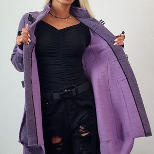Pode incluir: Um casaco comprido roxo com um exterior texturizado e um forro roxo mais claro. O casaco tem uma gola entalhada e &eacute; preso com bot&otilde;es pretos. A modelo est&aacute; vestindo um top preto e jeans pretos rasgados.