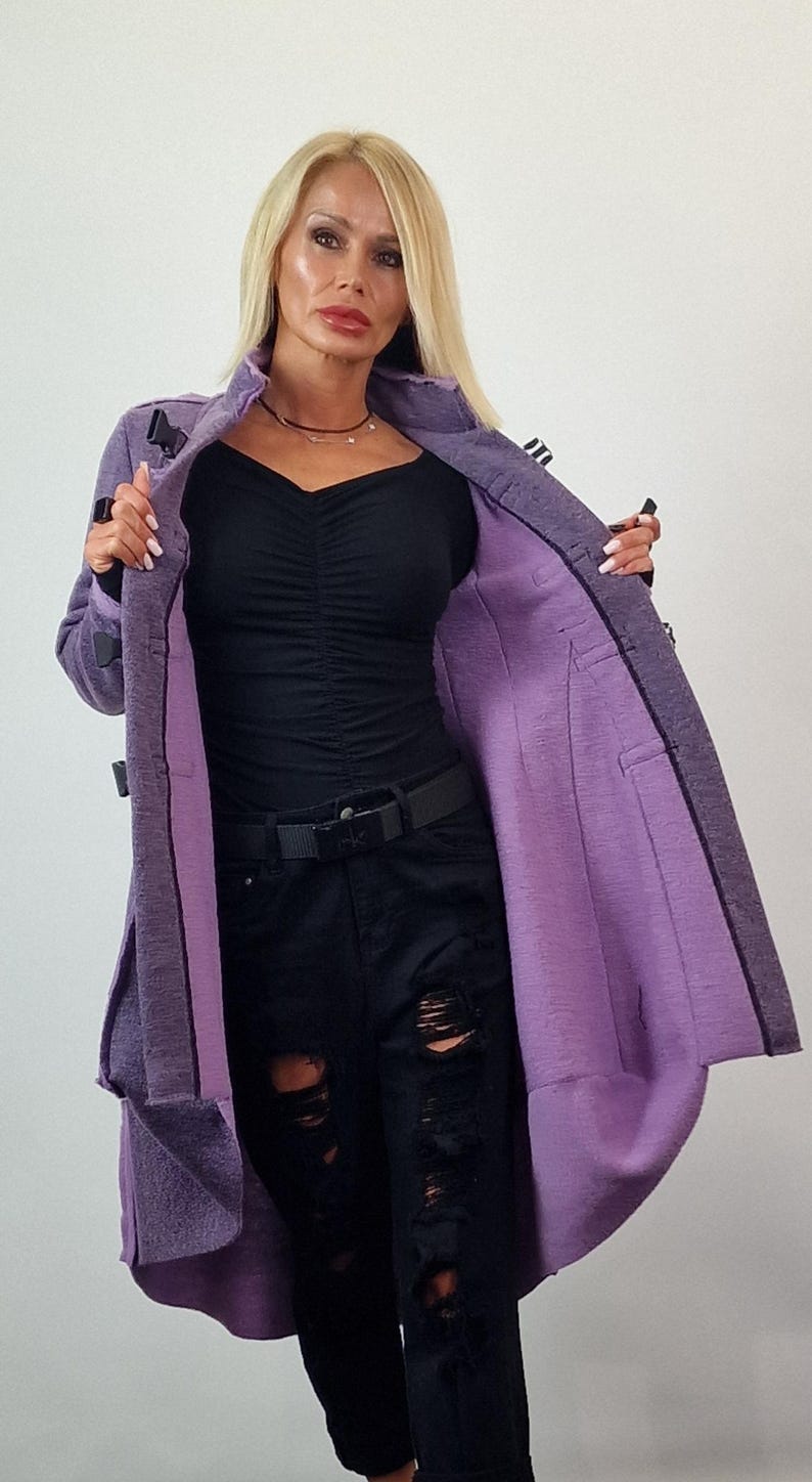 Pode incluir: Um casaco comprido roxo com um exterior texturizado e um forro roxo mais claro. O casaco tem uma gola entalhada e &eacute; preso com bot&otilde;es pretos. A modelo est&aacute; vestindo um top preto e jeans pretos rasgados.