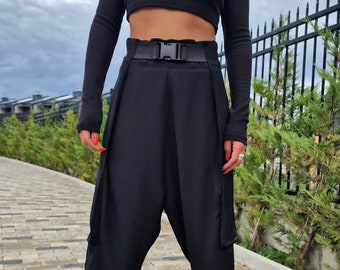 May include: A woman wearing a black long-sleeved crop top with the text "SERIOUSSTYLE" printed on the front, black trousers with a buckle belt, and black and white trainers. She is wearing a black beret with silver studs and sunglasses.