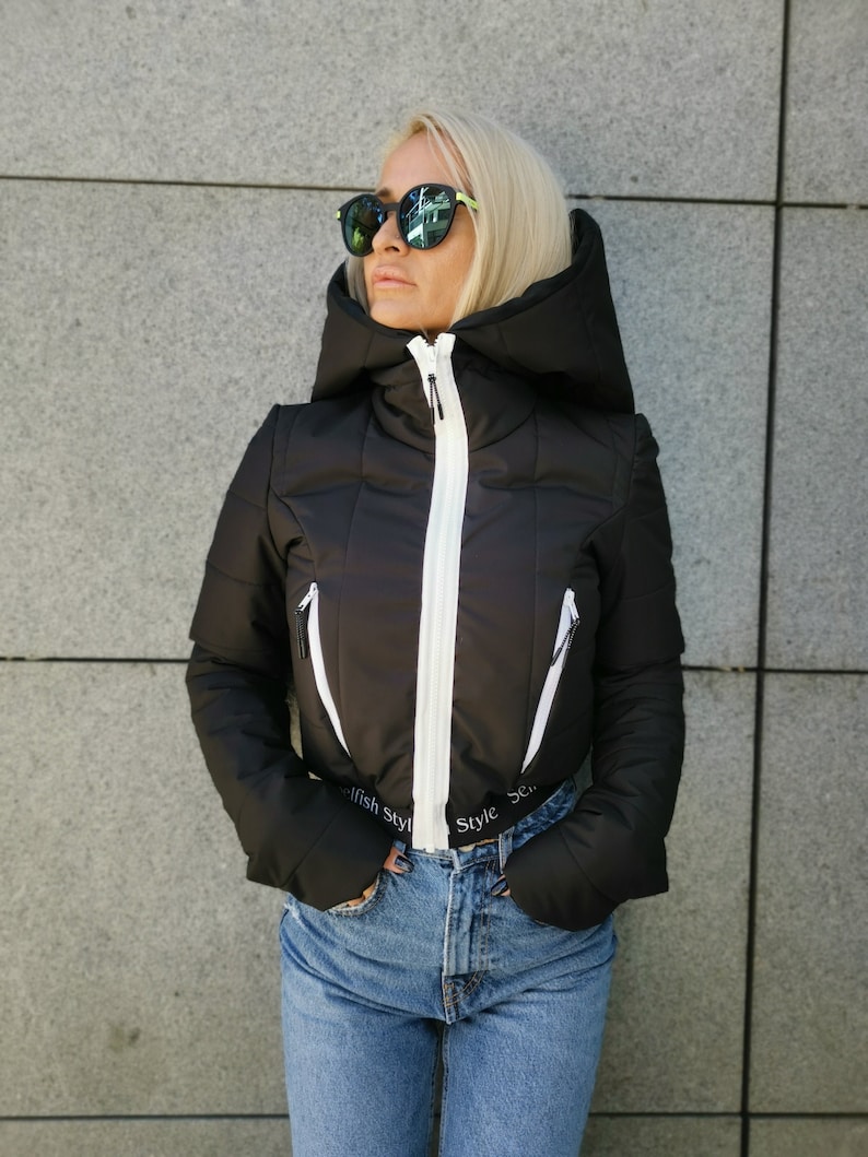May include: A black puffer jacket with a white zip and white trim. The jacket has a hood and the text "Selfish Style" is printed on the bottom.