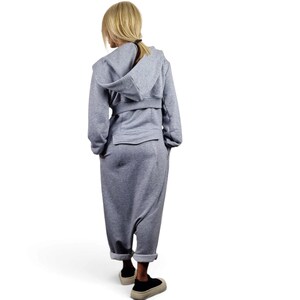 May include: A heather gray hooded jumpsuit featuring long sleeves, a belted waist detail, and a loose-fitting pant leg that tapers at the ankle. The garment includes a hood and a horizontal seam across the back, finished with black sneakers.
