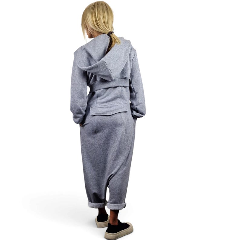 May include: A heather gray hooded jumpsuit featuring long sleeves, a belted waist detail, and a loose-fitting pant leg that tapers at the ankle. The garment includes a hood and a horizontal seam across the back, finished with black sneakers.