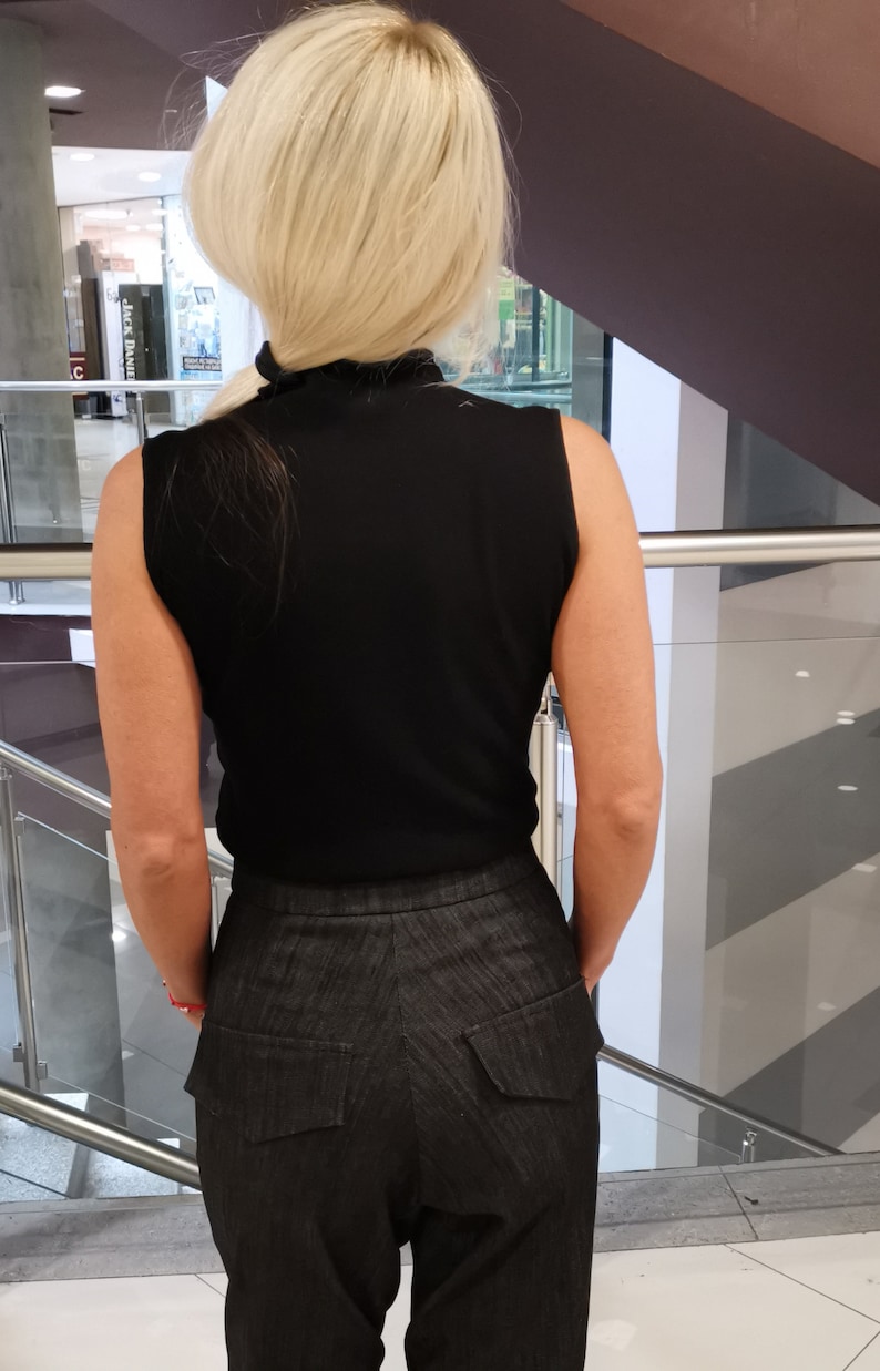 May include: A black sleeveless mock neck shirt and dark gray pants with large pockets in the back.