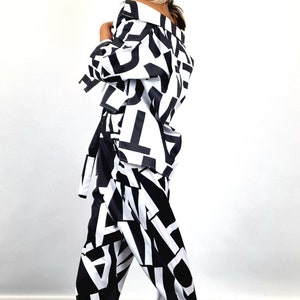 May include: A black and white patterned pantsuit with a black beret and sunglasses. The pantsuit features a bold, abstract print of letters and shapes.