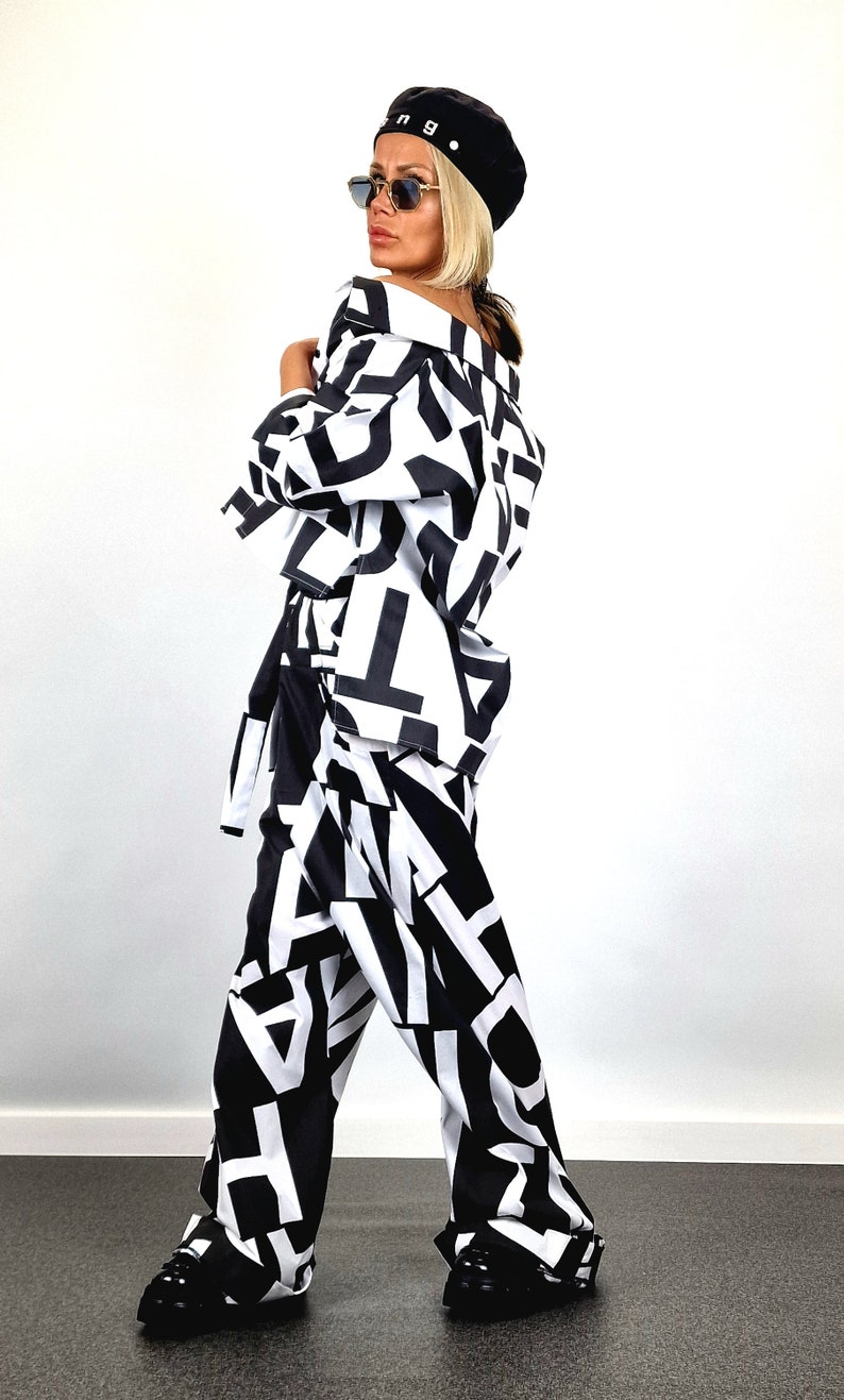 May include: A black and white patterned pantsuit with a black beret and sunglasses. The pantsuit features a bold, abstract print of letters and shapes.