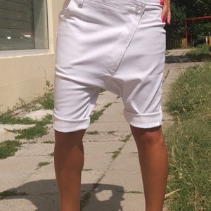 K&ouml;nnte beinhalten: Wei&szlig;e Baumwollshorts mit einem einzigartigen asymmetrischen Design und umgeschlagenen S&auml;umen. Die Shorts werden mit wei&szlig;en Sneakers mit einem schwarzen "CHANEL"-Logo getragen.