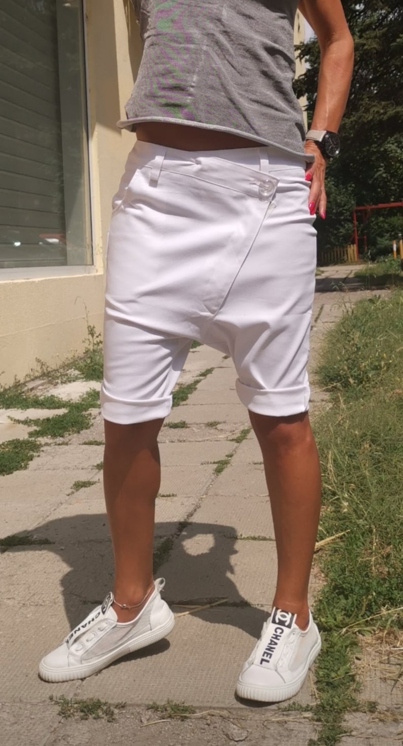 K&ouml;nnte beinhalten: Wei&szlig;e Baumwollshorts mit einem einzigartigen asymmetrischen Design und umgeschlagenen S&auml;umen. Die Shorts werden mit wei&szlig;en Sneakers mit einem schwarzen "CHANEL"-Logo getragen.