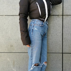 May include: A black puffer jacket with a white zip and white trim. The jacket has a hood and a  "Stylish Style" label on the bottom. The model is wearing blue jeans with distressed details and black heeled boots with fringe.