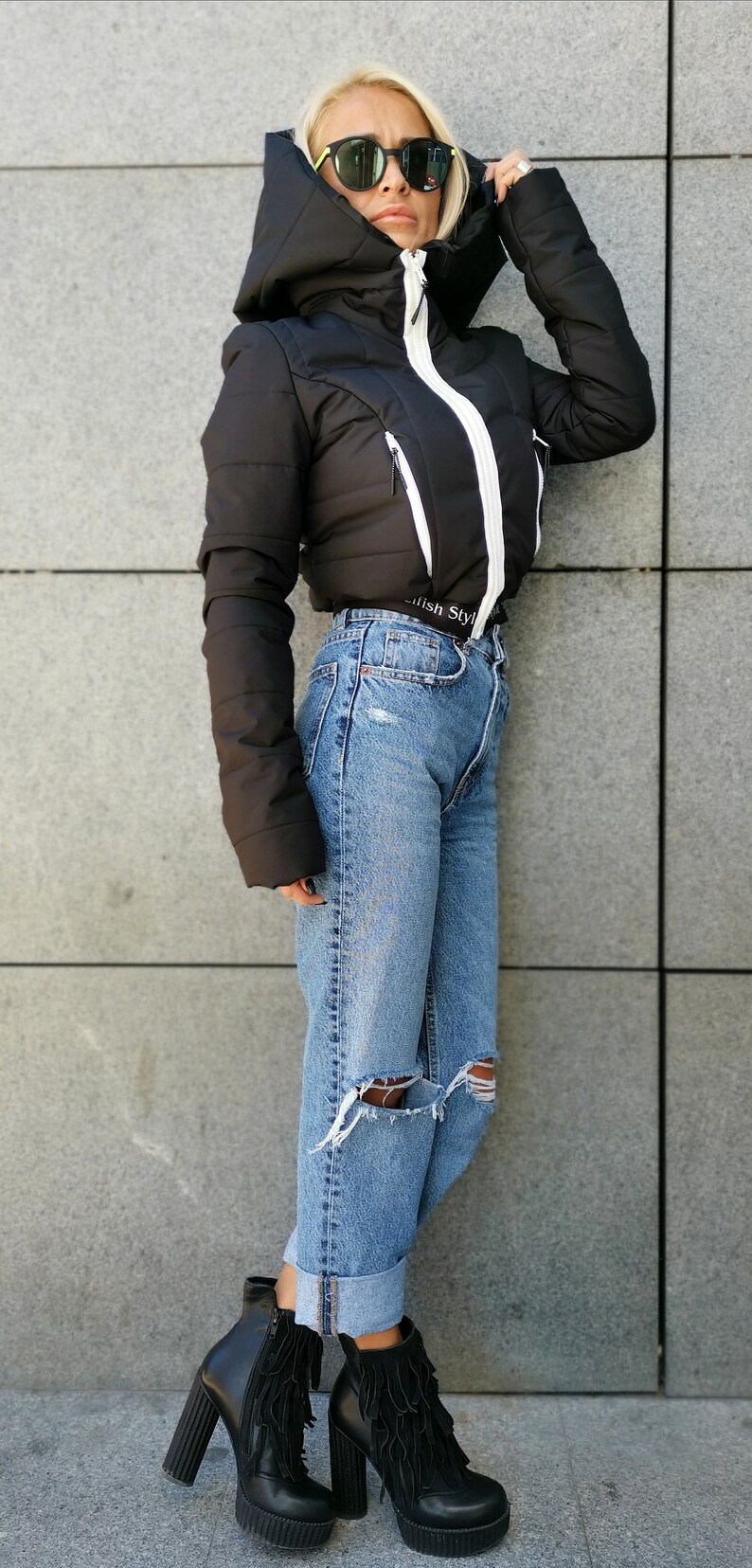 May include: A black puffer jacket with a white zip and white trim. The jacket has a hood and a  "Stylish Style" label on the bottom. The model is wearing blue jeans with distressed details and black heeled boots with fringe.